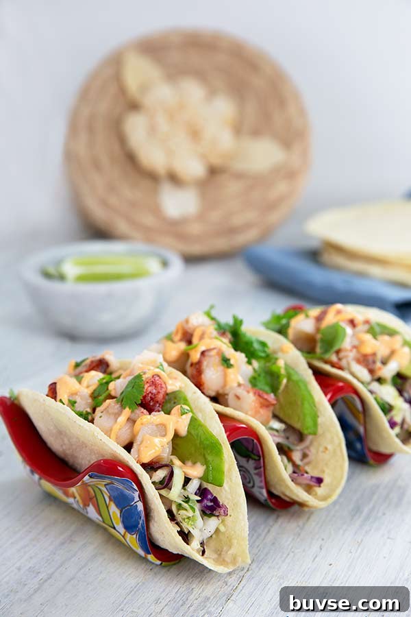 Lobster Tacos with Cilantro Slaw set in a taco holder that has a Mexican art pattern on it on a light gray wood table
