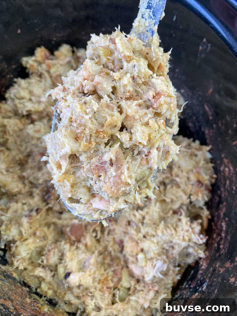 Large serving spoon holding a serving of dressing with chicken, celery and seasoned bread cubes over a slow cooker full
