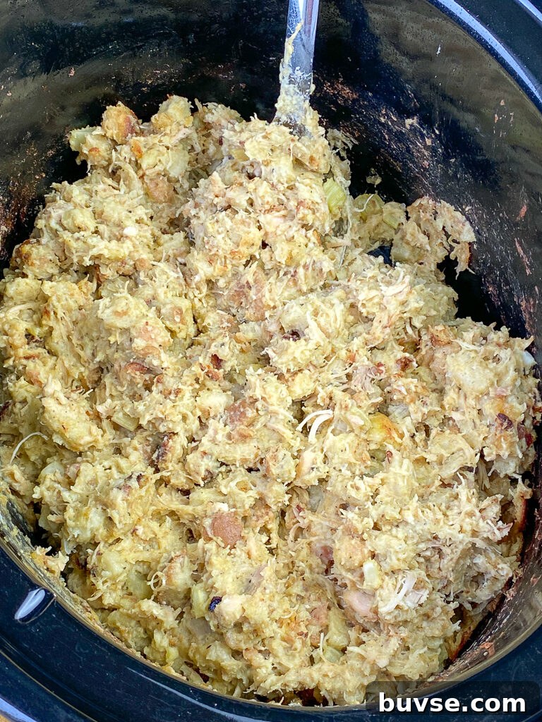 Large black crock pot full of dressing with shreds of chicken for more flavor