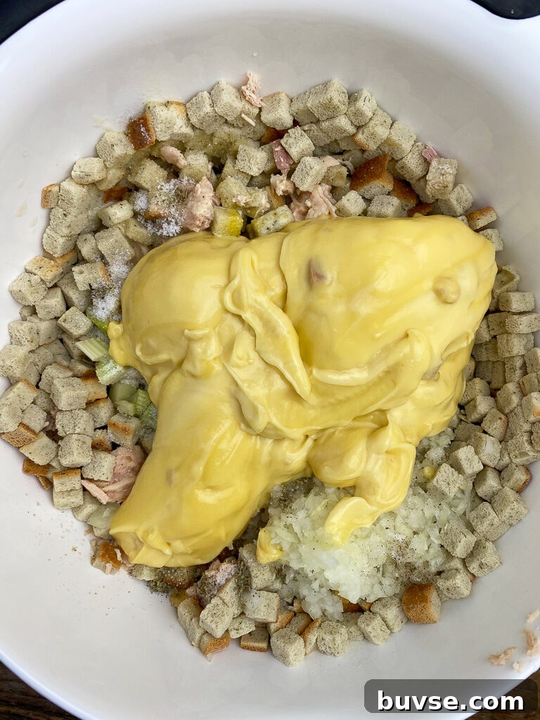 Two cans of cream of chicken soup poured on herb seasoned bread cubes in a white mixing bowl
