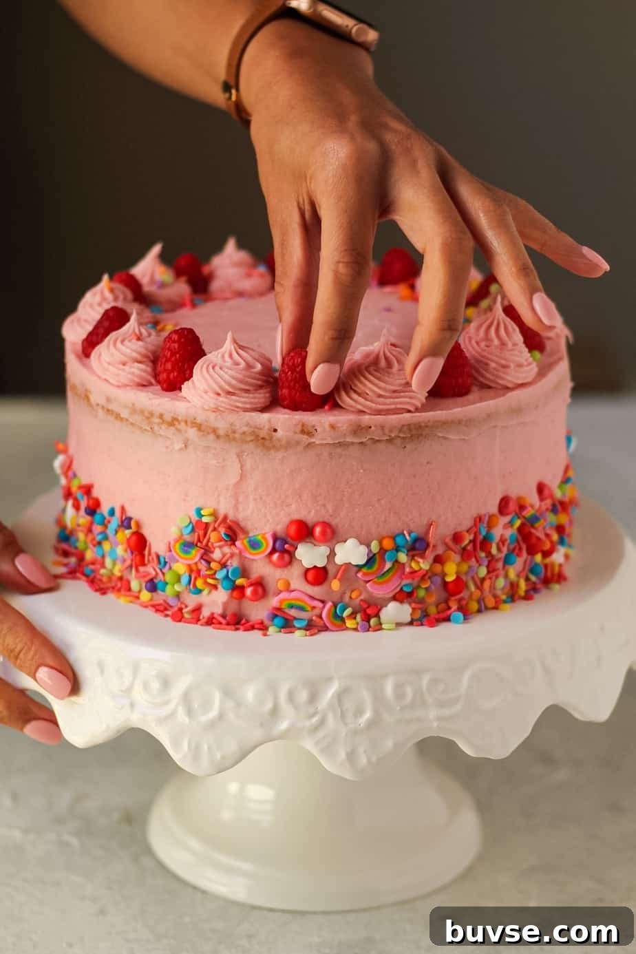 Lemon Raspberry Birthday Cake Recipe 5 hand placing raspberry on lemon raspberry birthday cake
