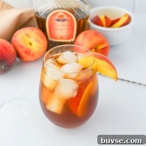 Glass filled with ice, peach whiskey, and tea, on a white marble table.