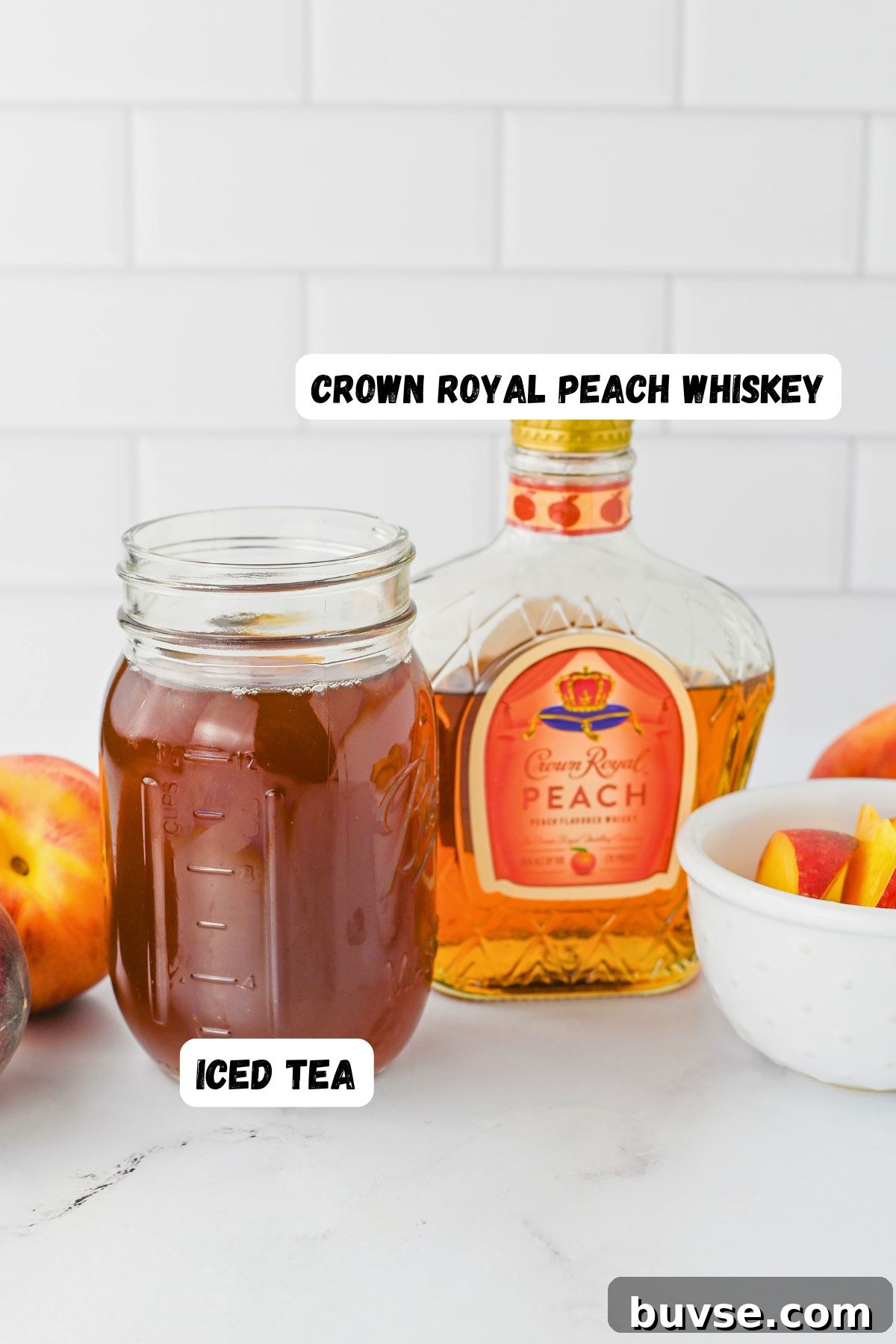Royal Peach Iced Tea Recipe 3 Bottle of whiskey and mason jar of tea, on a marble table with fresh peaches in a small white bowl.