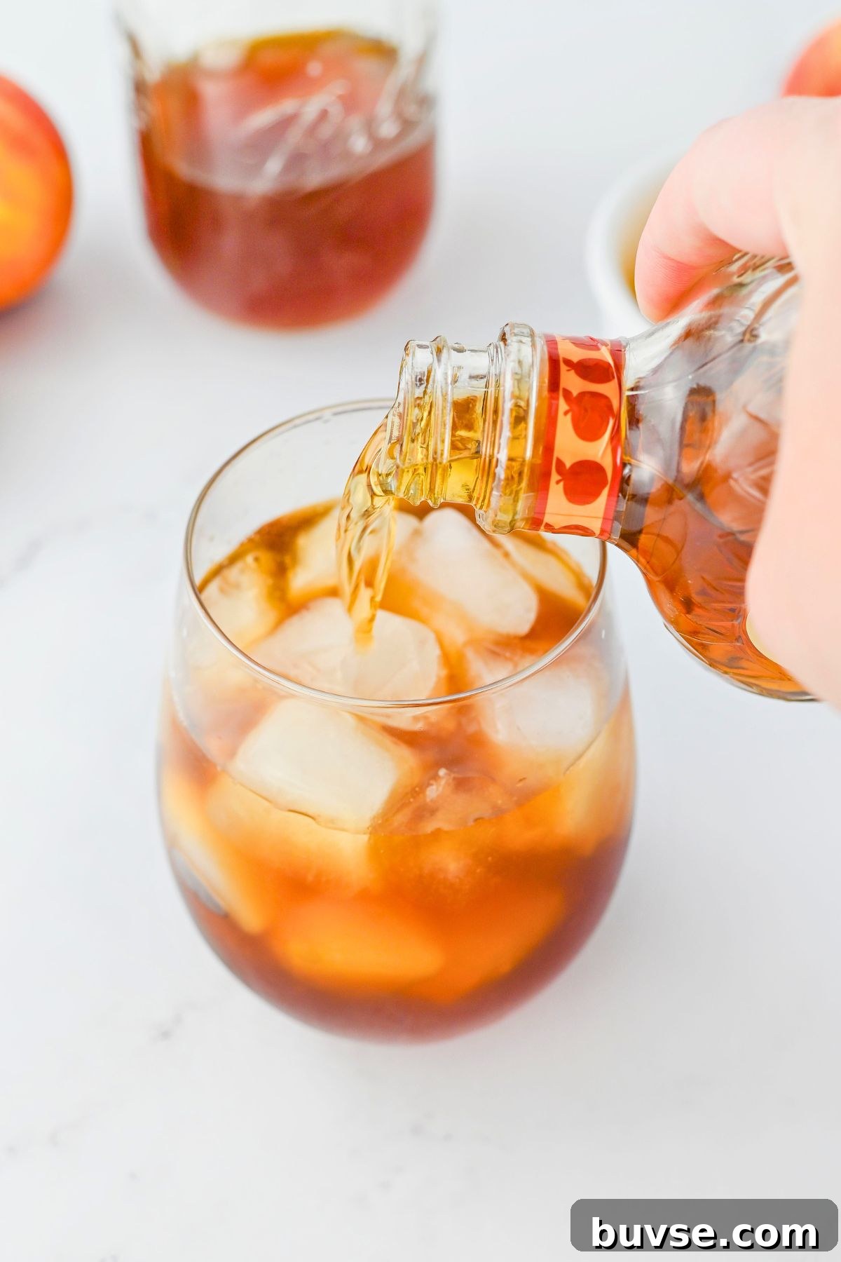 Royal Peach Iced Tea Recipe 4 Peach whiskey and tea being mixed together in a small glass filled with ice.