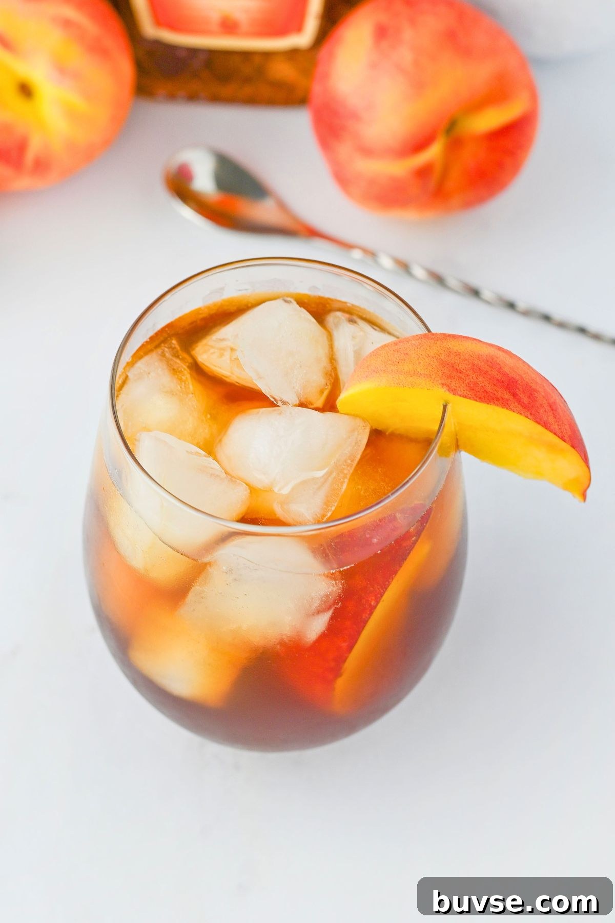 Royal Peach Iced Tea Recipe 5 A small glass with ice whiskey and tea, garnished with a fresh peach slice.
