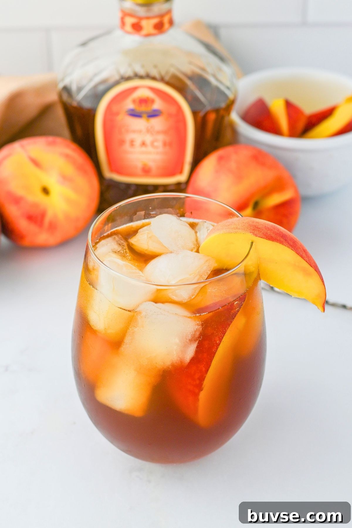 Royal Peach Iced Tea Recipe 6 A small glass with ice whiskey and tea, garnished with a fresh peach slice.