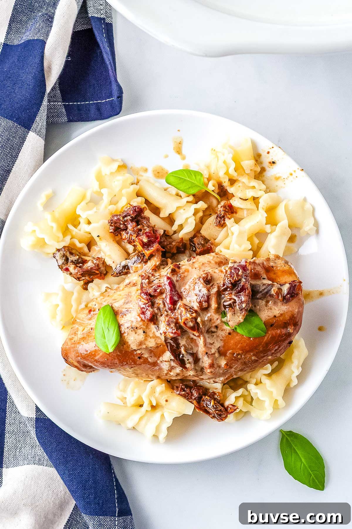 Crockpot Marry Me Chicken served over pasta with a creamy Parmesan sauce, sun-dried tomatoes, and fresh basil.