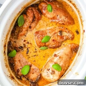 Creamy Crockpot Marry Me Chicken cooking in a slow cooker with Parmesan sauce, sun-dried tomatoes, and fresh basil garnish.