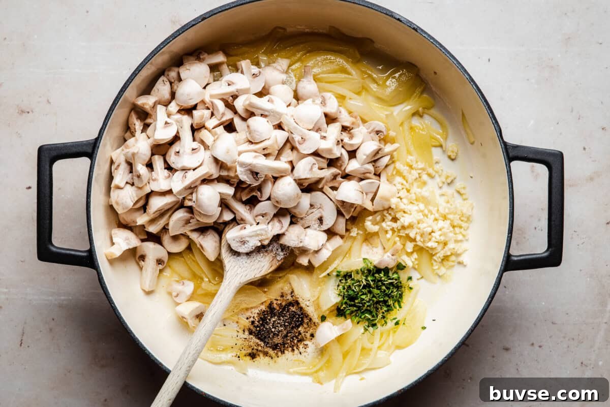 A large pot contains sliced onions, chopped mushrooms, minced garlic, chopped herbs, black pepper, and oil or butter, with a wooden spoon resting inside. The ingredients are ready to be cooked.