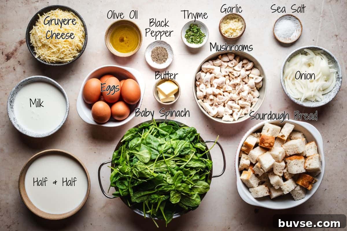 A top-down view of ingredients for a savory bread pudding recipe, including Gruyere cheese, olive oil, black pepper, thyme, garlic, sea salt, mushrooms, onion, milk, eggs, butter, baby spinach, half & half, and cubed sourdough bread.