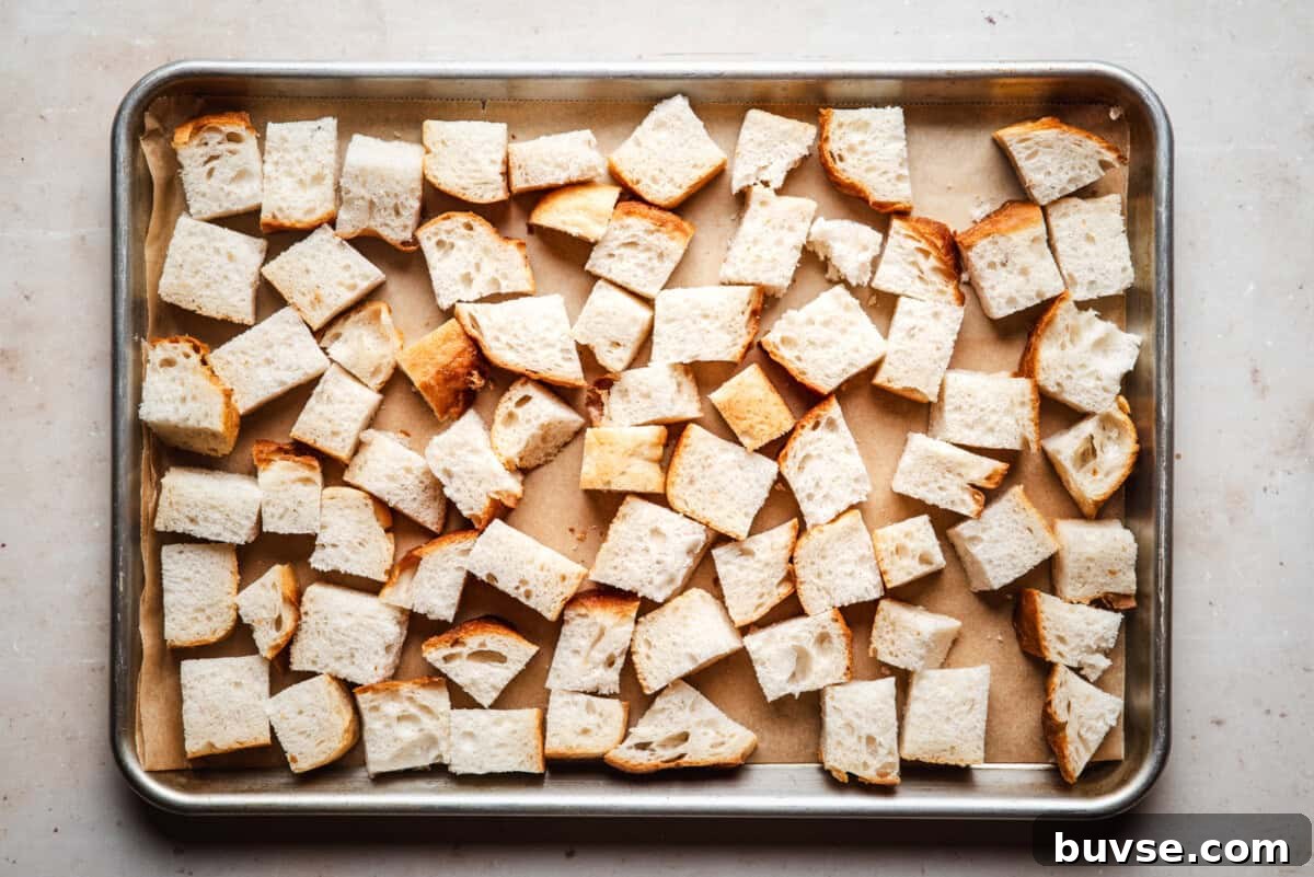 A baking tray lined with parchment paper holds evenly spread cubes of sliced bread, ready for toasting or baking.