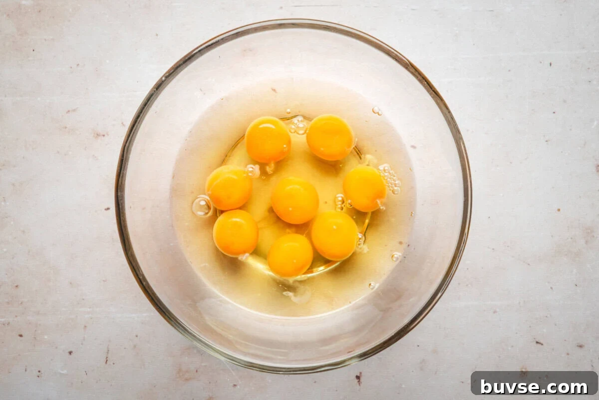 A glass bowl containing seven raw eggs with unbroken yolks, placed on a light-colored surface.