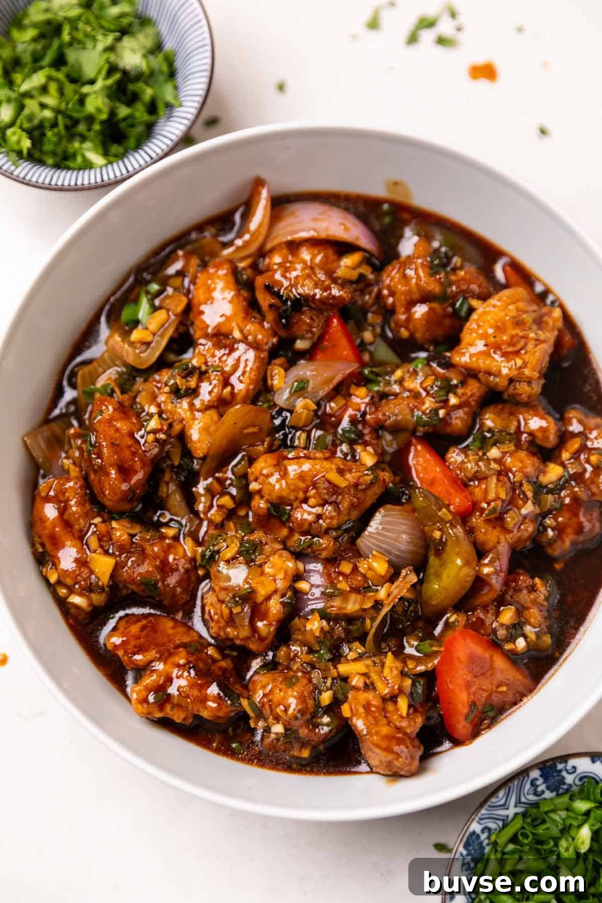 Authentic Street Style Chicken Manchurian 2 chicken manchurian served in a white bowl accompanied with garnishings