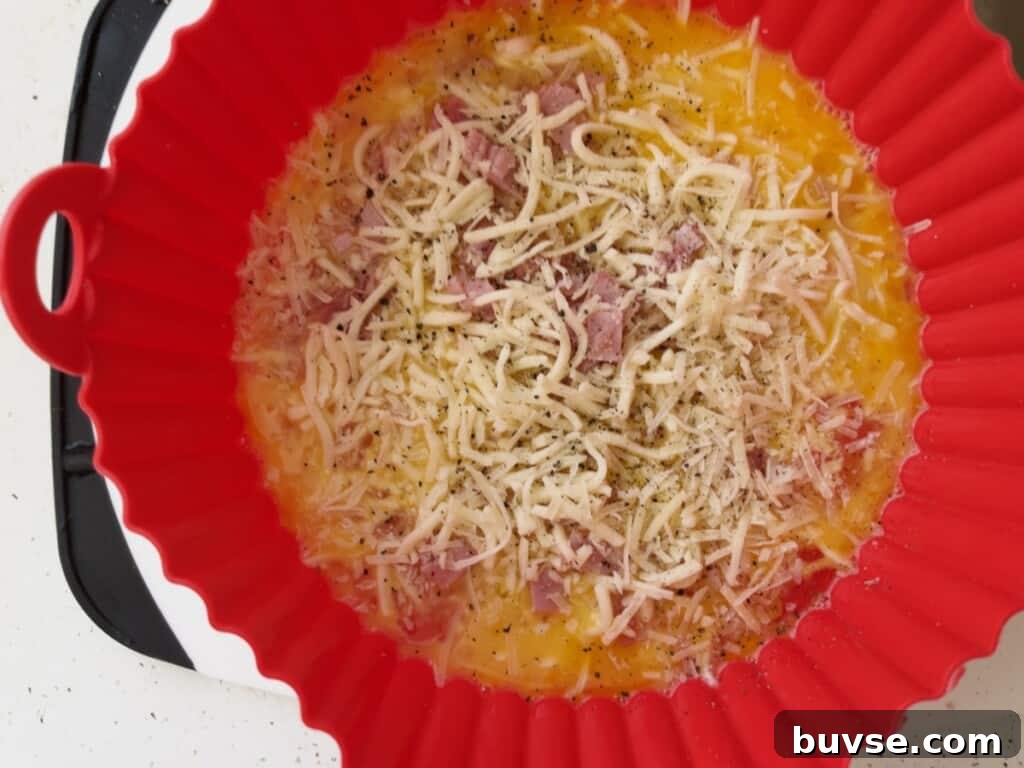 preparing air fryer ham and cheese omelet and adding ham and cheese to scrambled eggs