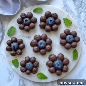 Chocolate Covered Blueberry clusters arranged in a flower shape on a round marble plate, garnished with fresh mint leaves.