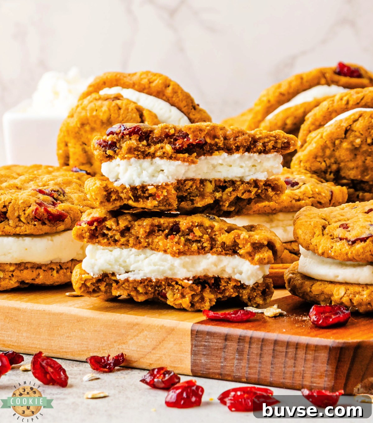 Pumpkin Oatmeal Sandwich Cookies with Cranberry Filling 7 Soft pumpkin oatmeal cookies with dried cranberries and creamy frosting filling stacked on a wooden cutting board.