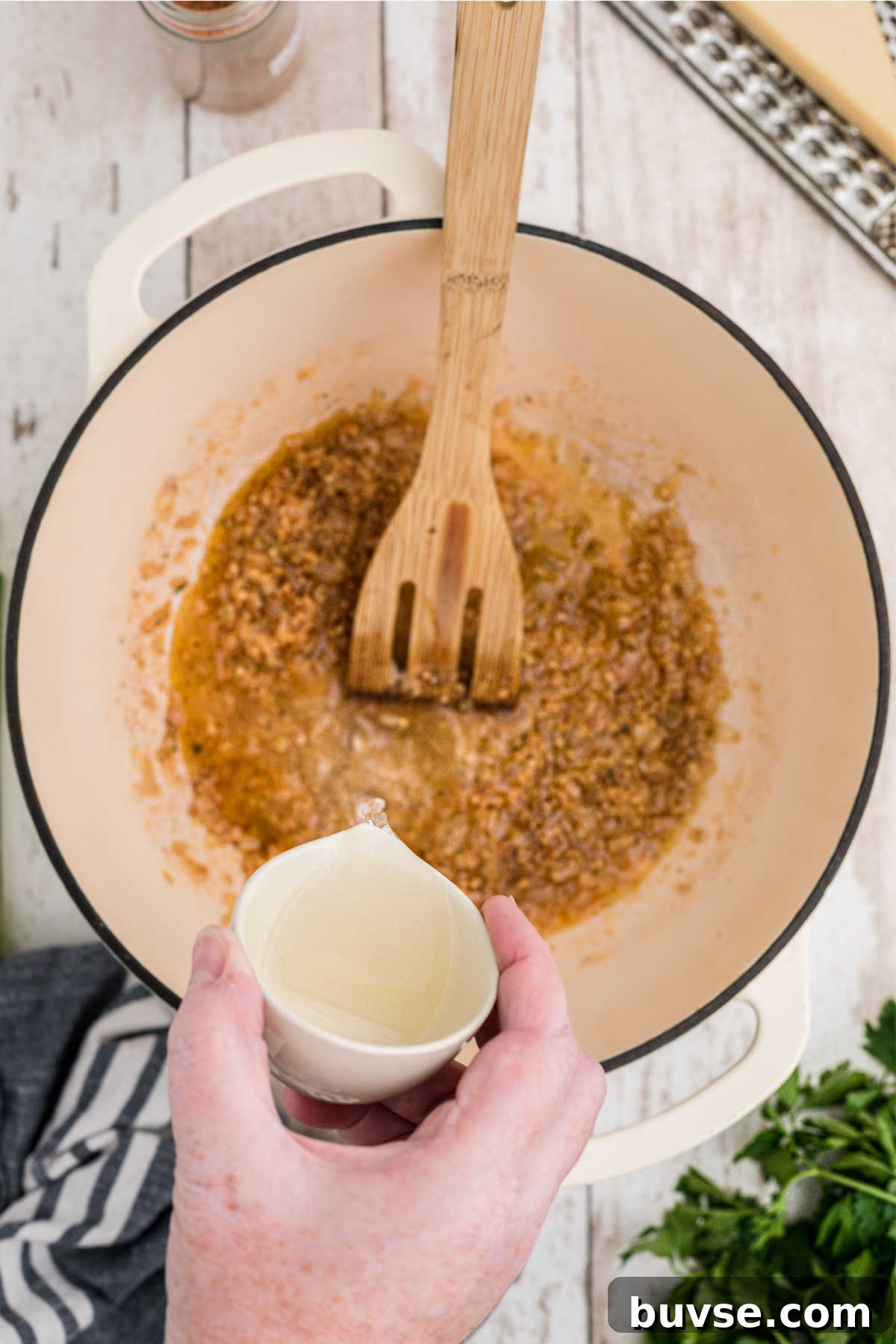 White wine being added to a pot with seasoned vegetables.