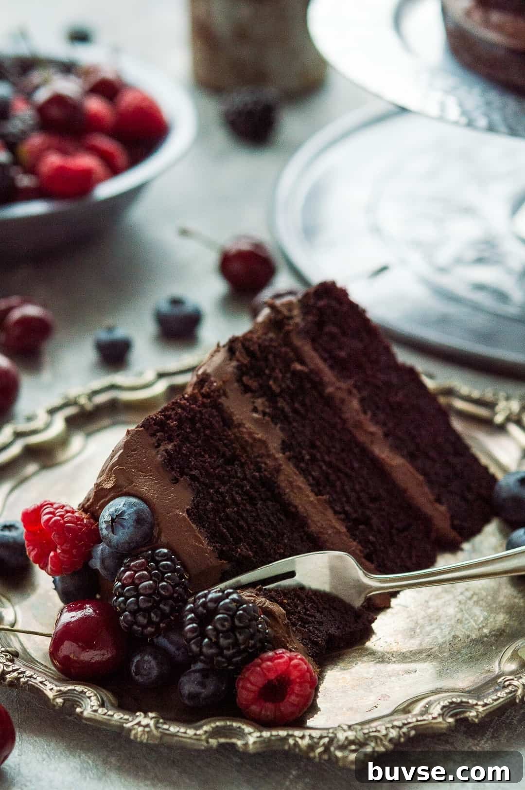 A slice of vegan chocolate fudge cake with coconut milk ganache topped with berries on a pewter plate.
