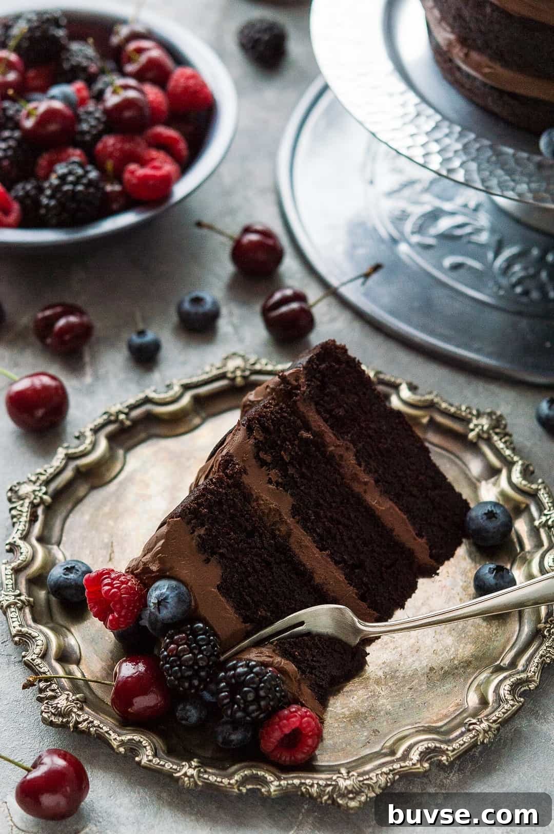Slice of easy vegan chocolate cake with vegan ganache on a pewter platter with fresh berries.