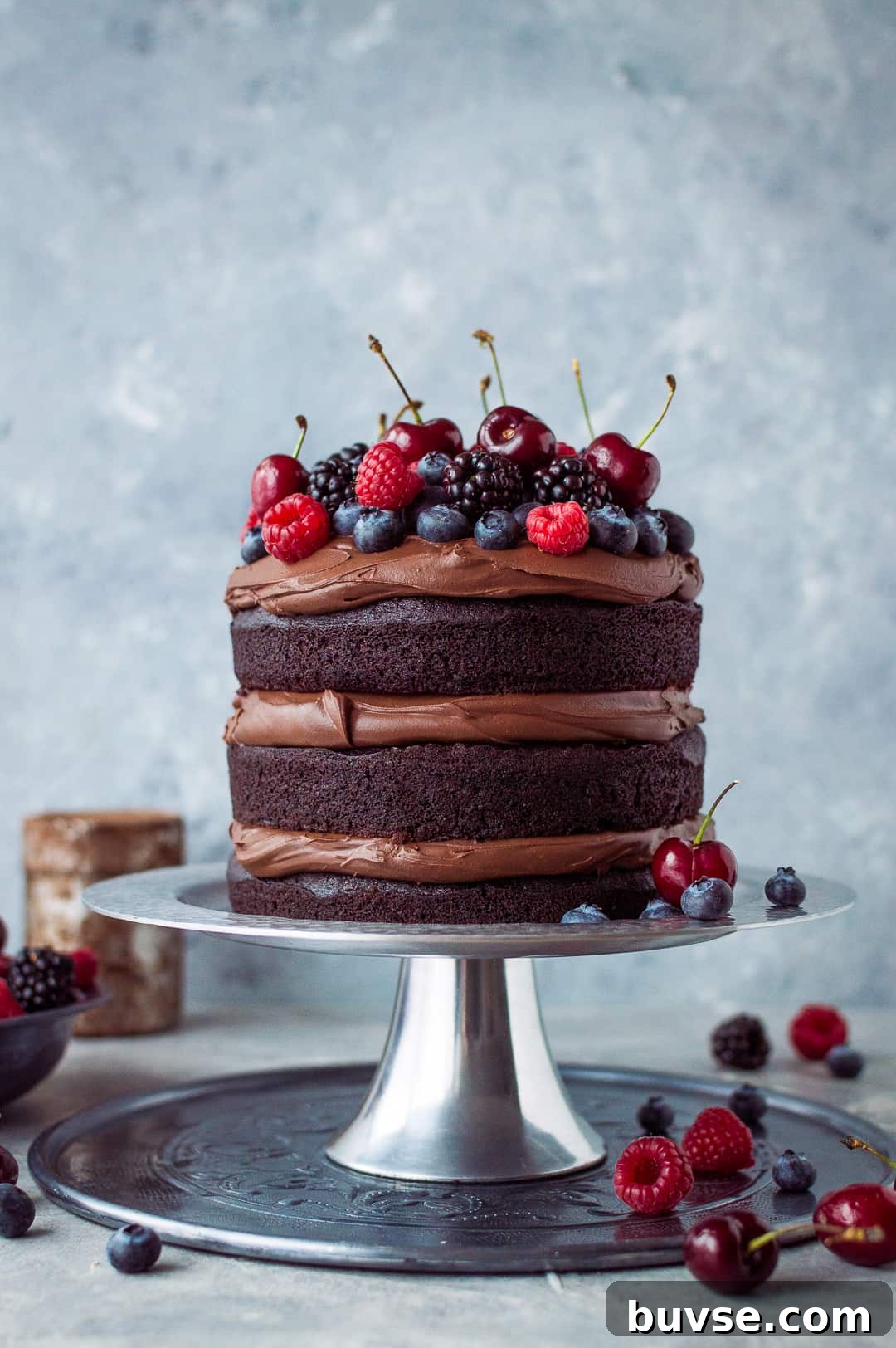 Vegan chocolate fudge cake with coconut milk ganache and fresh berries on a silver cake stand.
