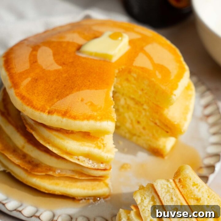A white plate with a stack of pancakes with self rising flour topped with a pat of butter and drizzled with syrup. A fork is taking a bite from the stack. The plate is on a tan counter with a jar of syrup.