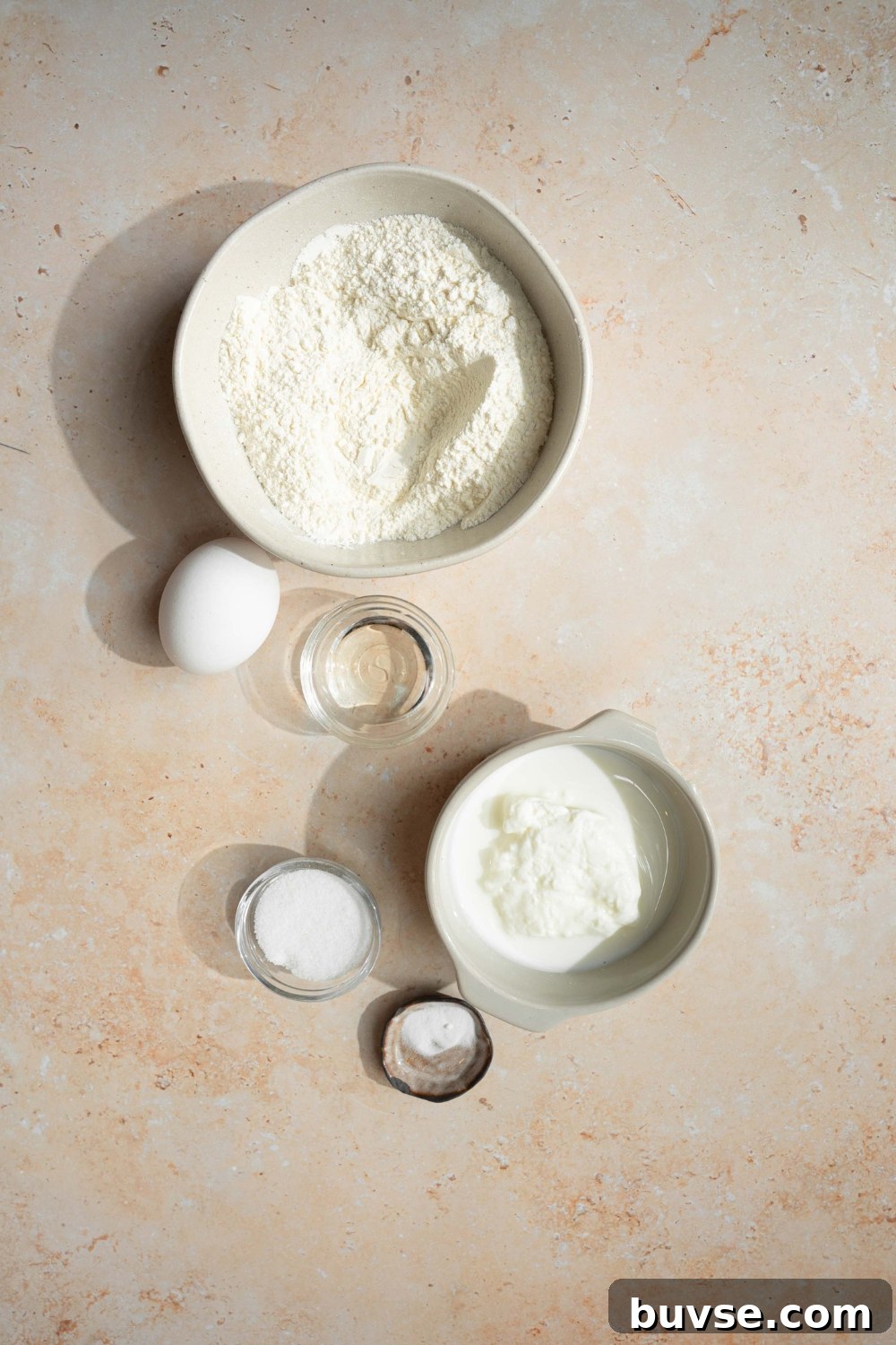 An overhead shot of several bowls in various sizes containing ingredients to make pancakes with self rising flour including self rising flour, sugar, baking soda, milk, and eggs.