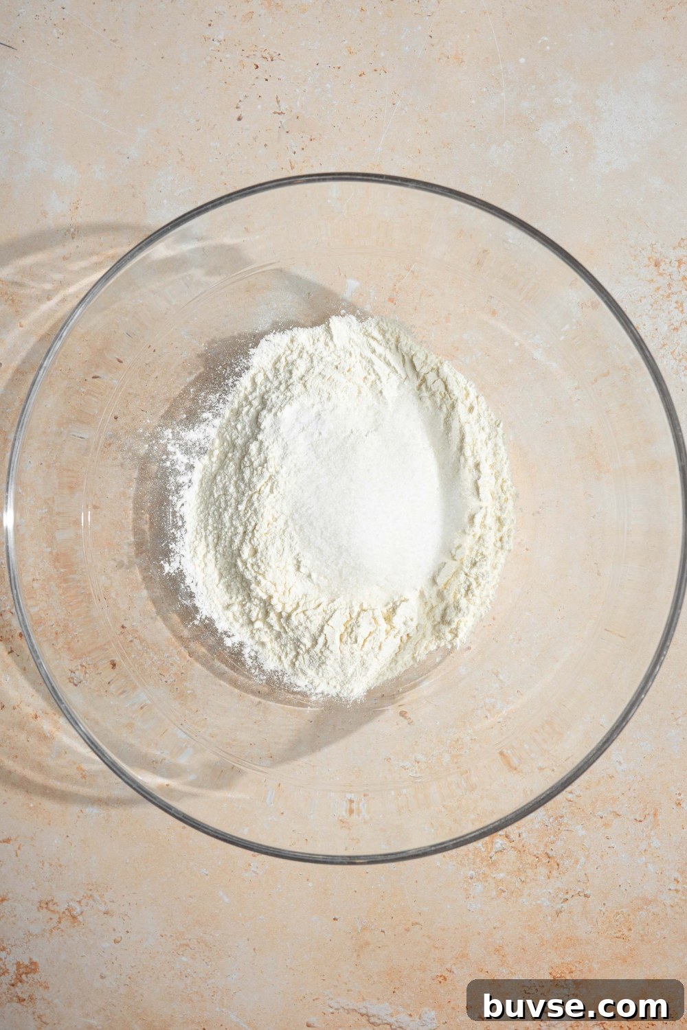 A large glass bowl with ingredients to make pancakes including self rising flour, sugar, and baking soda.