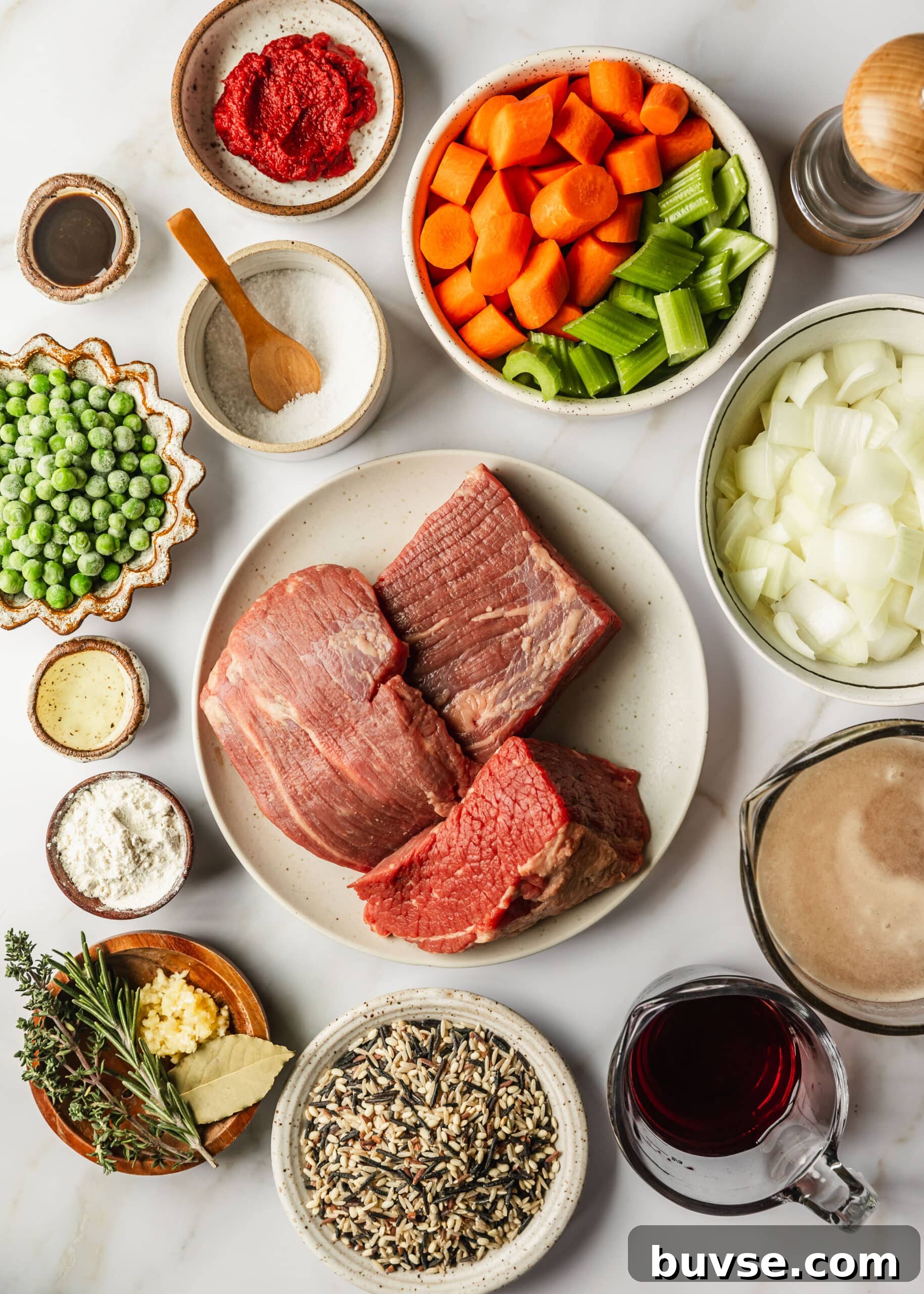 Slow-Cooked Brisket Stew with Wild Rice and Vegetables 3 White and brown bowls of beef, carrots, celery, onions, peas, oil, flour, herbs, garlic, wild rice, red wine, and beef broth on a white counter.