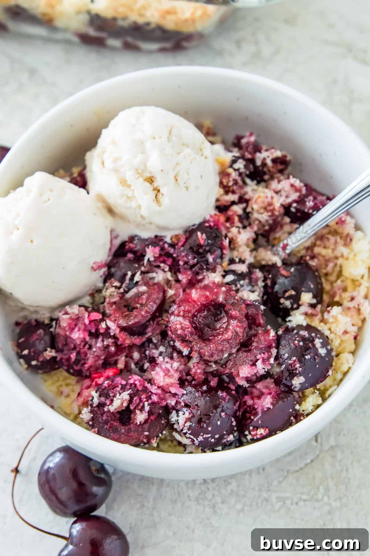 A bowl of cherry crisp with a spoon in it and two scoops of vanilla ice cream on it.
