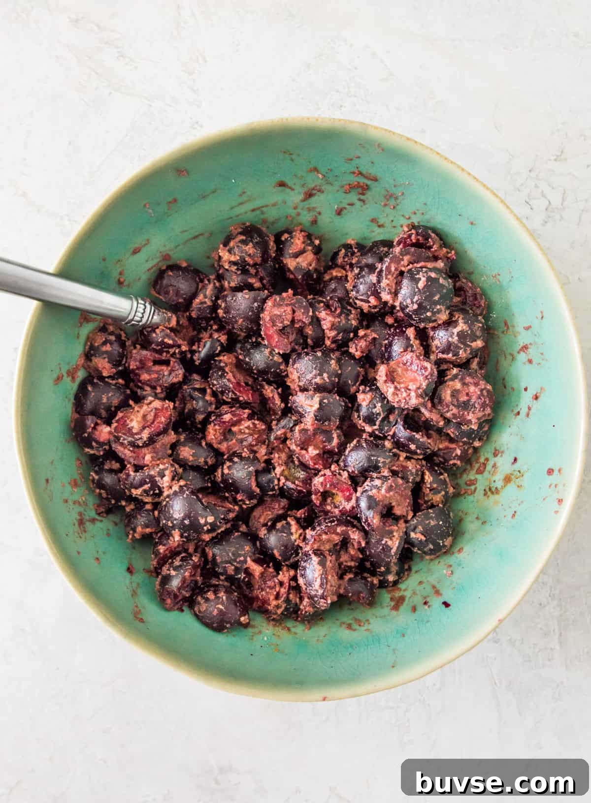 A bowl filled with chopped cherries with a spoon in them.
