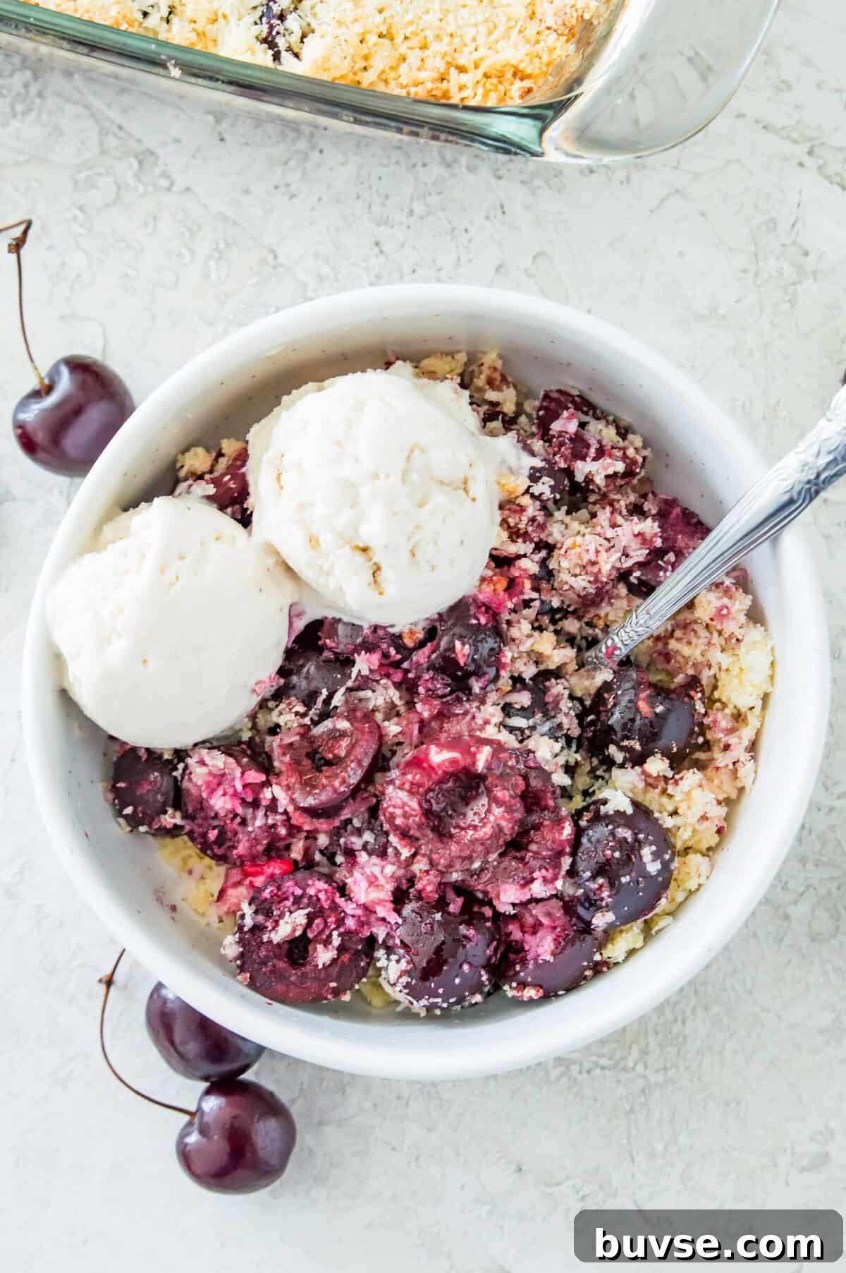 A bowl of cherry crumble with two scoops of vanilla ice cream on it and a spoon in it.