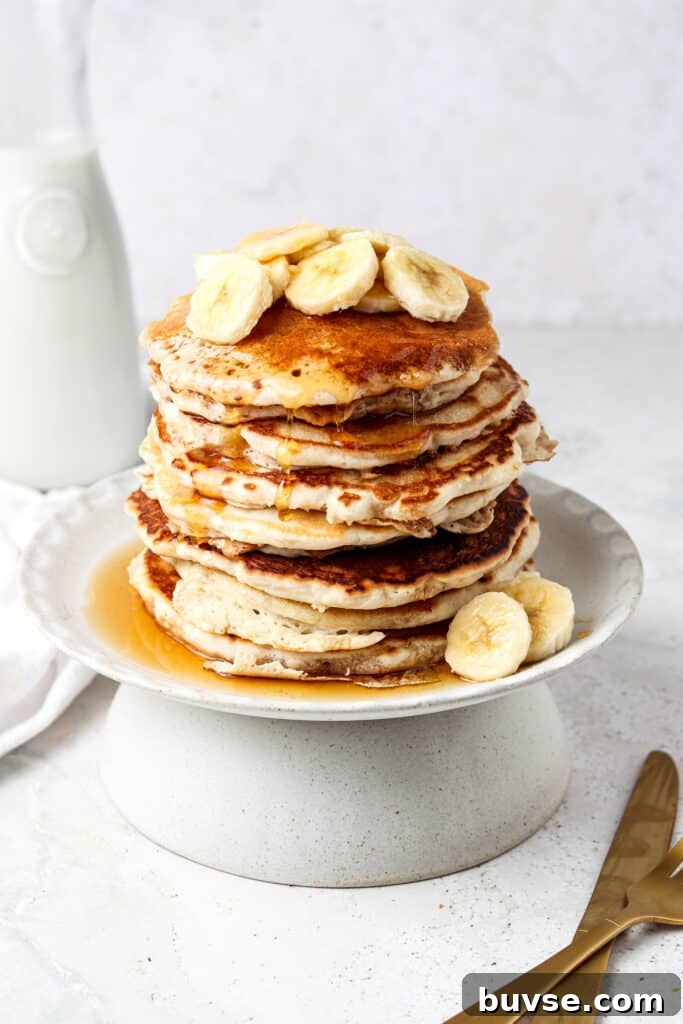3 ingredient protein pancakes stacked on a plate with bananas and maple syrup