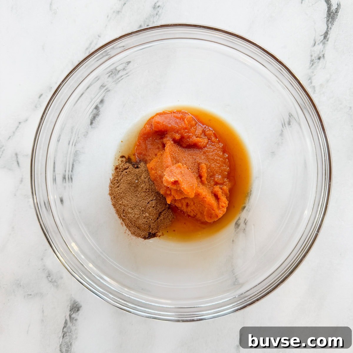 Spices, pumpkin, and maple syrup in a glass bowl.