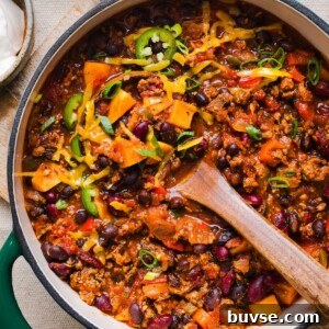 Healthy sweet potato turkey chili in a large pot, topped with shredded cheddar and green onions.