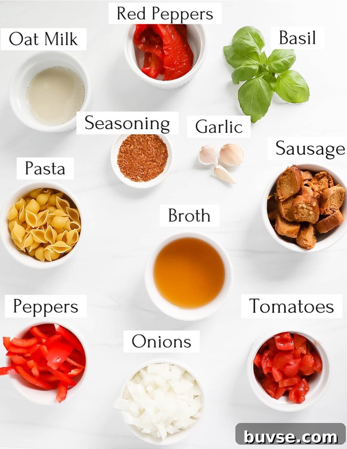 Creamy Vegan Cajun Pasta with Smoky Vegan Sausage 3 Labeled ingredients in small white bowls including: oat milk, red peppers, basil, seasoning, garlic, sausage, pasta, broth, peppers, tomatoes, onions.