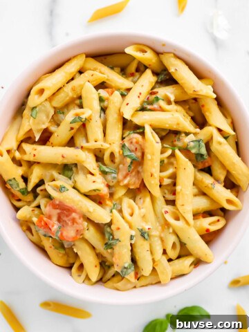 A pink bowl filled with penne pasta and creamy sauce.