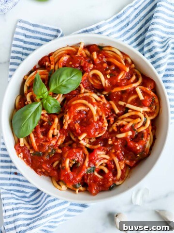 An overhead picture of a white bowl filled with spaghetti and red sauce, garnished with a sprig of basil.