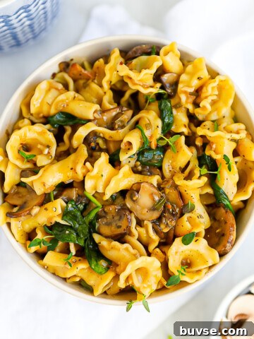 A round white bowl with mushroom pasta inside, garnished with fresh green herbs.