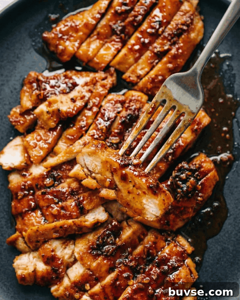 chicken breast cooked in a sticky brown sauce cut into strips on a black plate with a sticky sauce covered fork lifting a piece of chicken to the camera