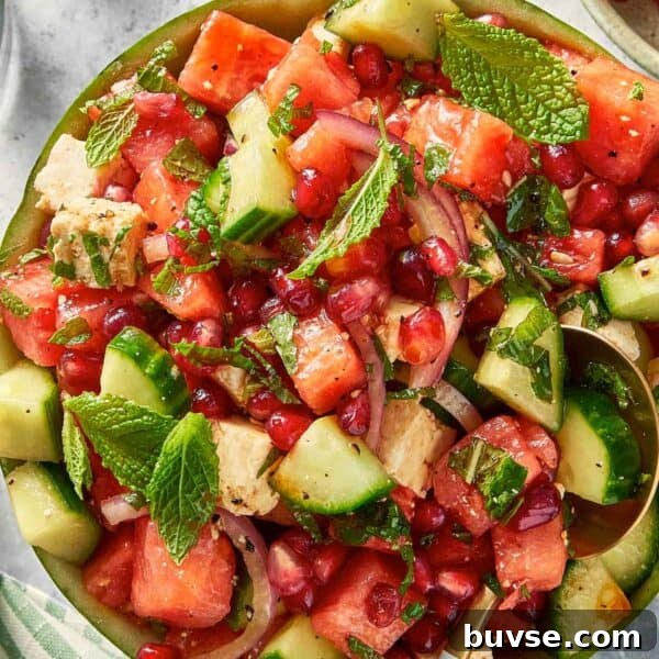 Top down view of watermelon feta salad with cucumber, red onion, and mint served inside a watermelon bowl with a serving spoon.
