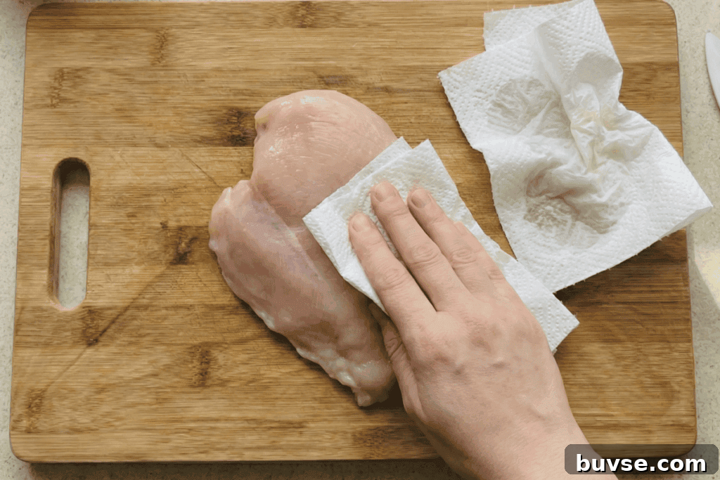 patting down a chicken breast over a wooden chopping board with paper towel