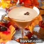 A pumpkin spice espresso martini garnished with three coffee beans, with fall leaves in the background.
