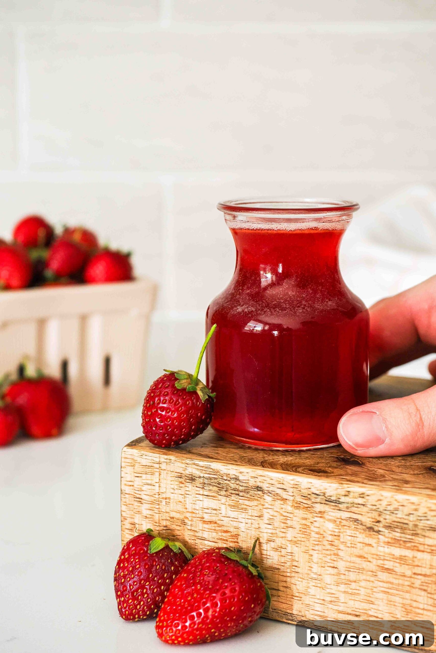 A hand holds a small jar of strawberry syrup.