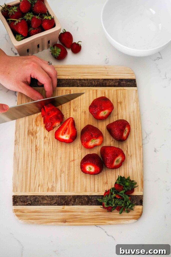 A knife dices strawberries on a wooden cutting board.