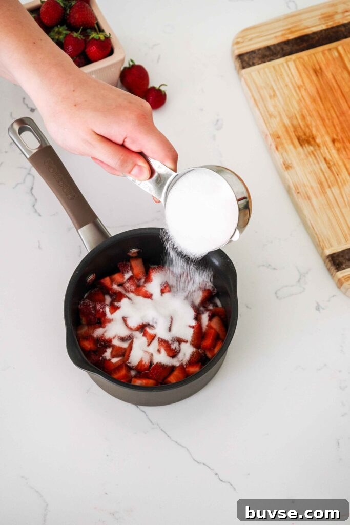 Sugar is poured onto diced strawberries in a small saucepan.