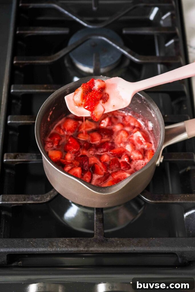 A spatula holds up softened strawberries in a small pot over the stove.