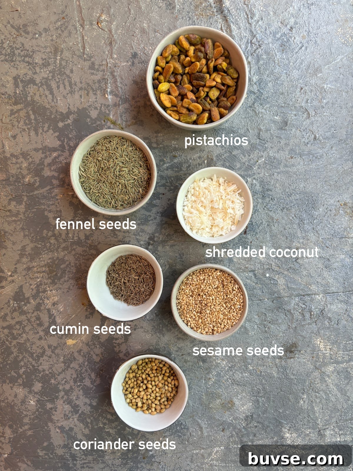 overhead image of the ingredients needed to make dukkah. Each ingredient is in its own small bowl and labeled with white text
