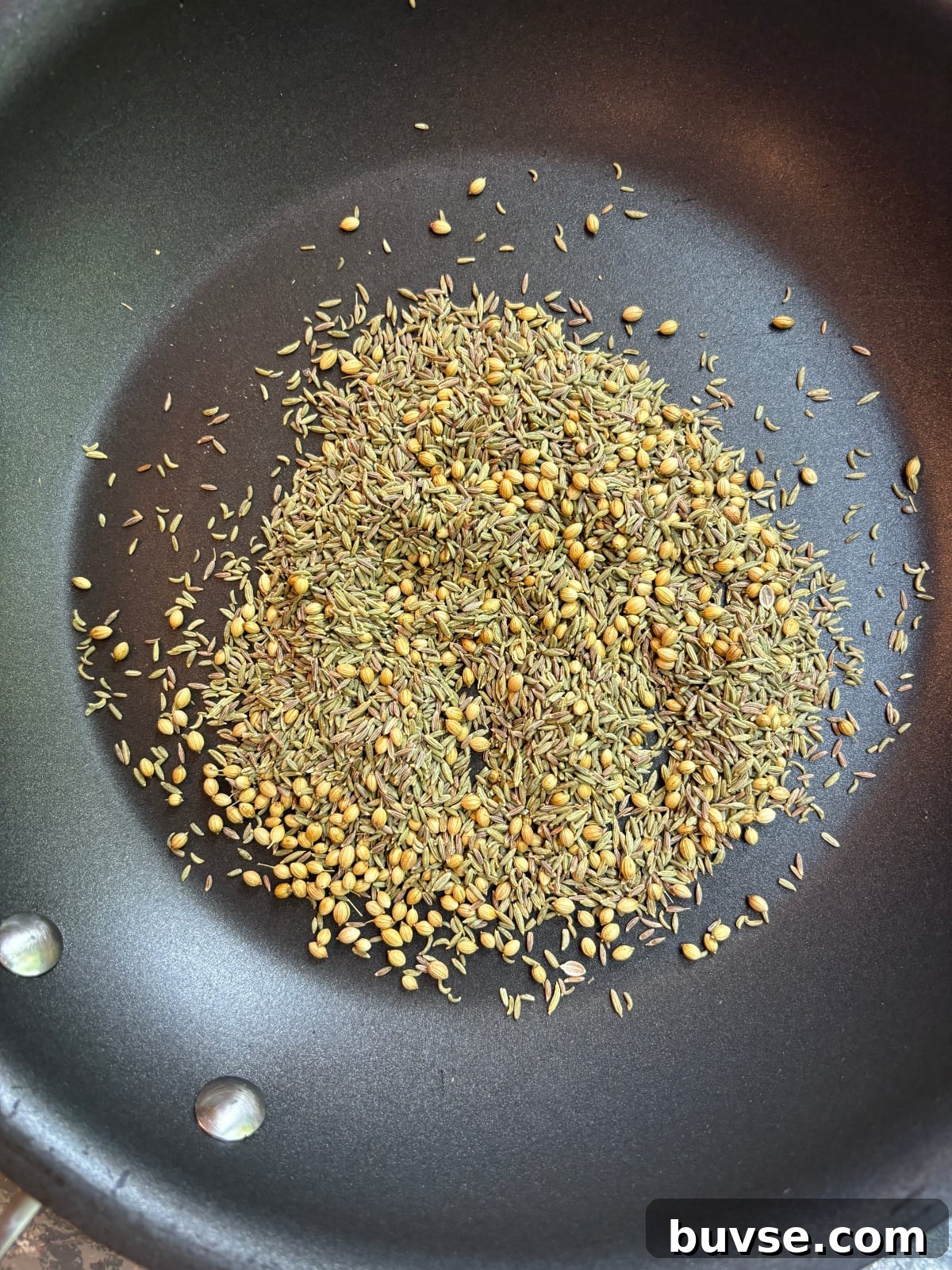 overhead image of fennel, cumin, and coriander seeds in a nonstick skillet