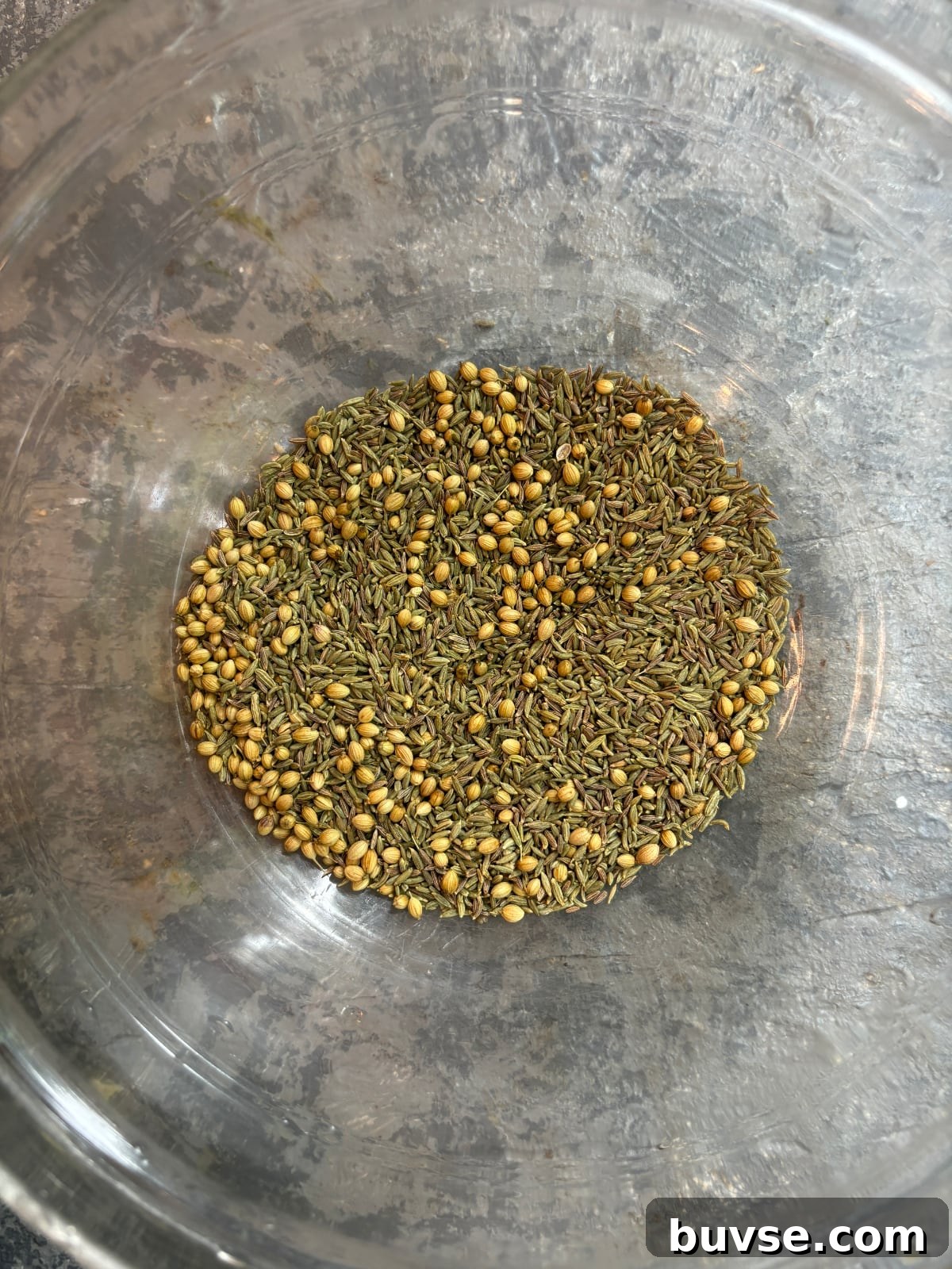 overhead image of fennel, cumin and coriander seeds in a clear glass mixing bowl