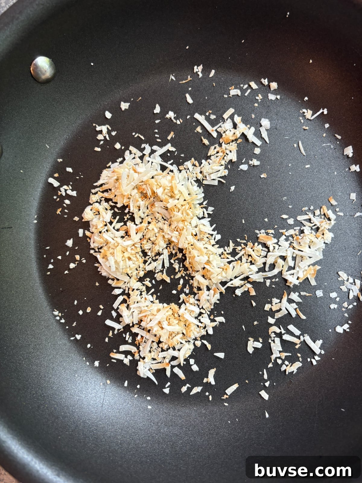 overhead image of shredded coconut being toasted in a nonstick skillet